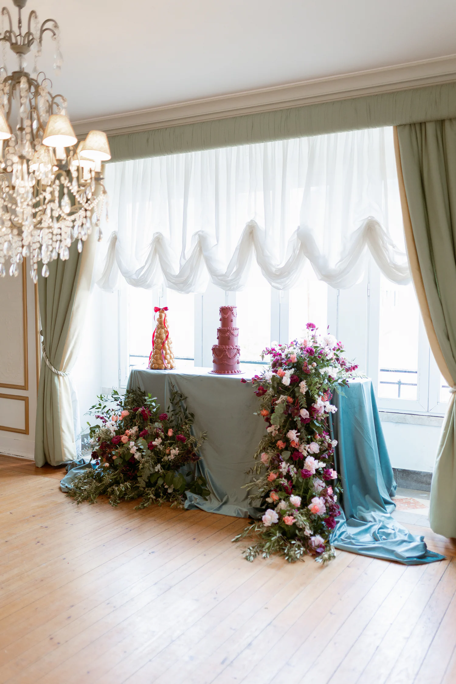 Mesa de bolo envolvida por flores em tons de ameixa e pêssego
